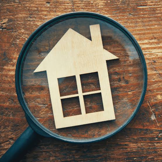 Magnifying glass over a wooden house cutout on a rustic wooden surface